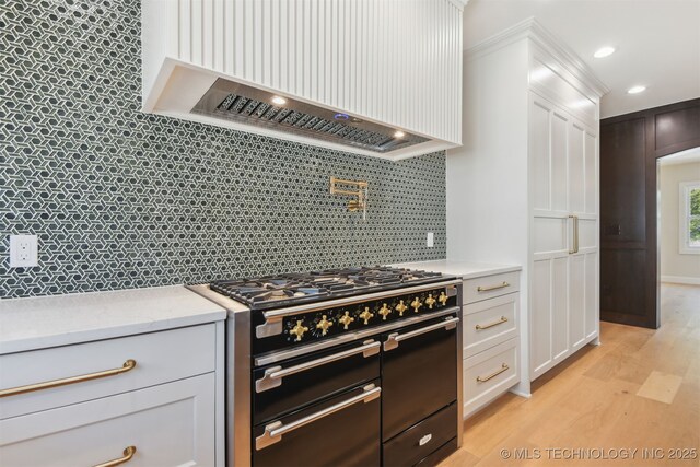 kitchen featuring custom exhaust hood, white cabinets, range with two ovens, light wood-style flooring, and backsplash