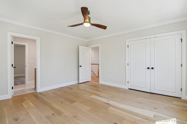 unfurnished bedroom with crown molding, light wood finished floors, a ceiling fan, baseboards, and a closet