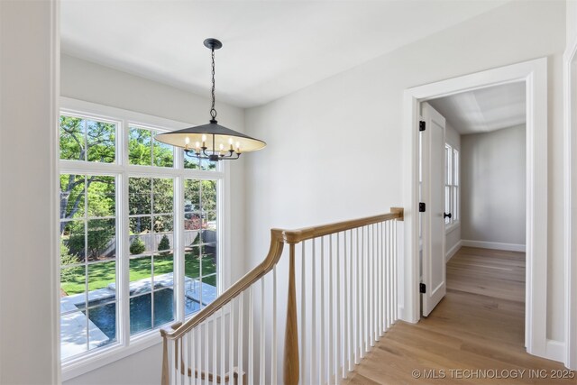hallway with an inviting chandelier, light wood finished floors, baseboards, and an upstairs landing