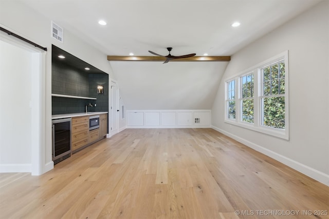 unfurnished living room with a ceiling fan, wet bar, visible vents, wine cooler, and light wood-style flooring