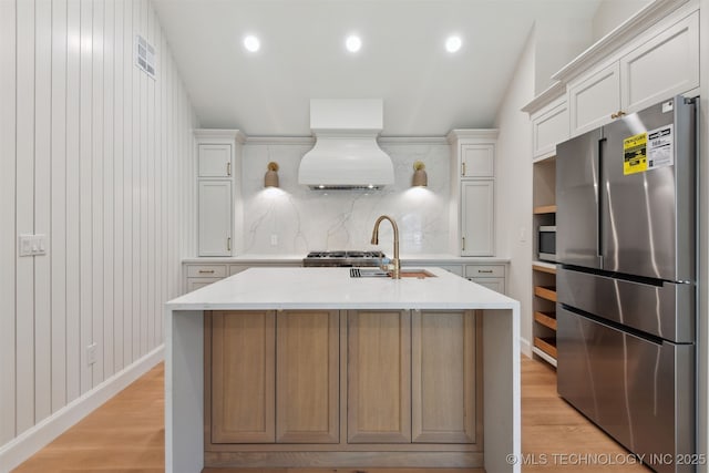kitchen featuring light wood-type flooring, appliances with stainless steel finishes, custom exhaust hood, and visible vents