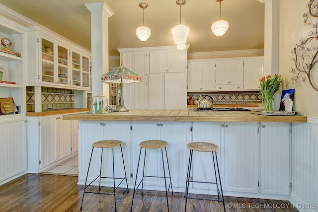 kitchen with decorative backsplash, stainless steel gas cooktop, wood finished floors, a breakfast bar, and white cabinets