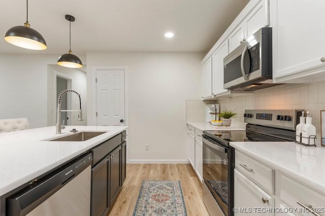 kitchen with appliances with stainless steel finishes, hanging light fixtures, a sink, light countertops, and white cabinetry