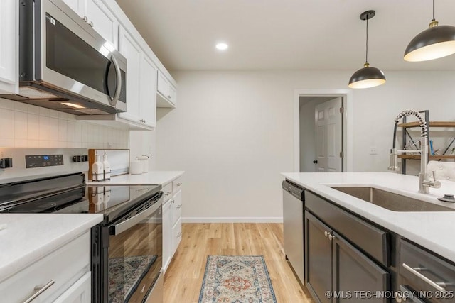 kitchen with light countertops, a sink, light wood finished floors, hanging light fixtures, and stainless steel appliances