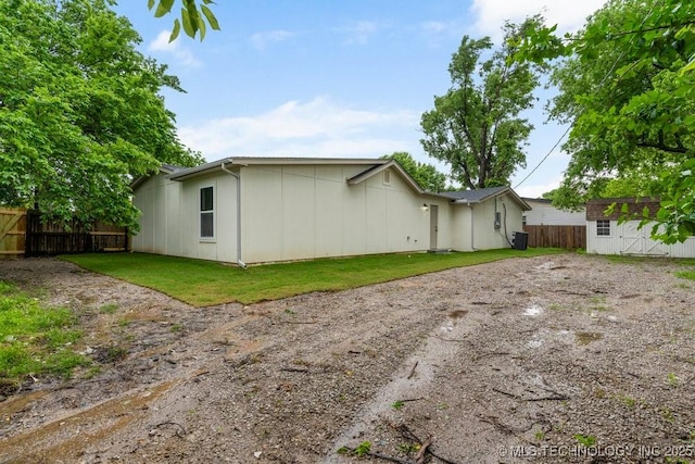 rear view of property featuring an outbuilding, central air condition unit, fence, a storage unit, and a yard