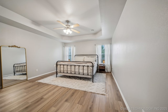 bedroom with baseboards, a tray ceiling, wood finished floors, and visible vents