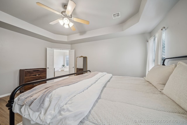 bedroom with a ceiling fan, visible vents, wood finished floors, a raised ceiling, and baseboards