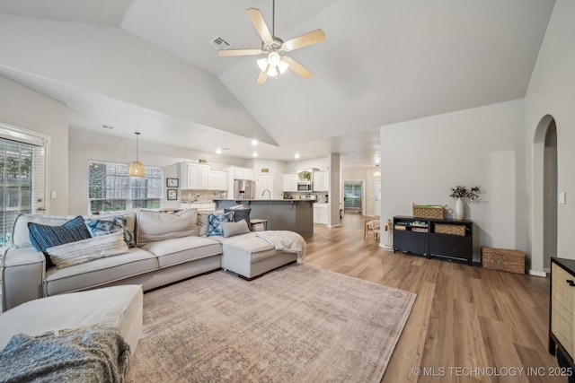 living room featuring visible vents, ceiling fan, high vaulted ceiling, arched walkways, and light wood finished floors