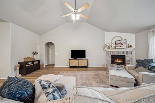 living area featuring a brick fireplace, wood finished floors, lofted ceiling, ceiling fan, and arched walkways