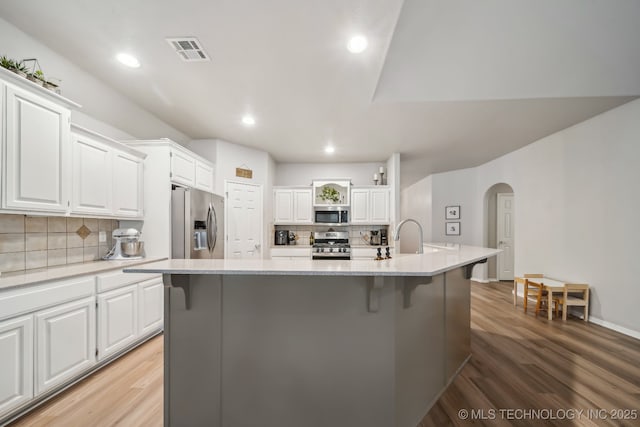 kitchen with decorative backsplash, visible vents, appliances with stainless steel finishes, arched walkways, and light wood-style floors