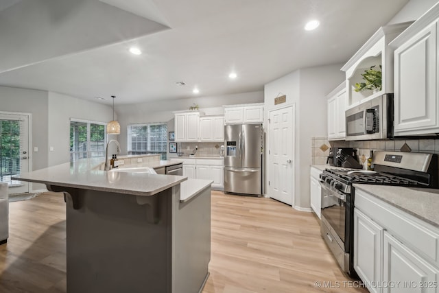 kitchen featuring decorative backsplash, white cabinets, a sink, light wood finished floors, and stainless steel appliances