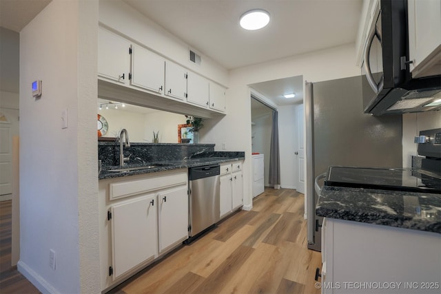 kitchen with washer / dryer, white cabinets, a sink, light wood finished floors, and dishwasher