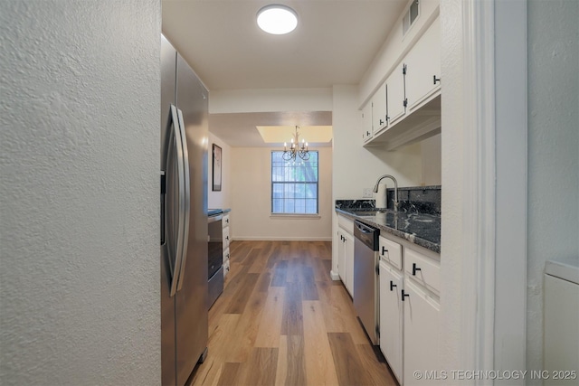 kitchen featuring white cabinets, a sink, light wood finished floors, a notable chandelier, and stainless steel appliances