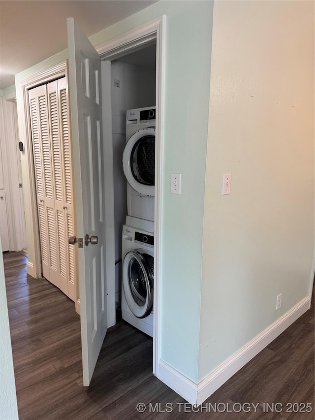 clothes washing area with dark wood-type flooring, laundry area, baseboards, and stacked washing maching and dryer