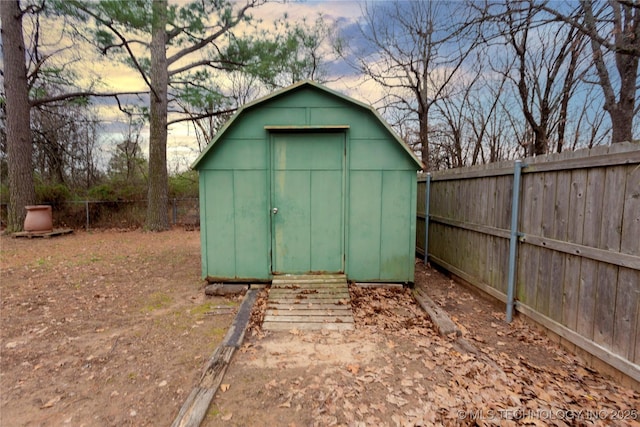 outdoor structure at dusk featuring a fenced backyard, an outdoor structure, and a shed