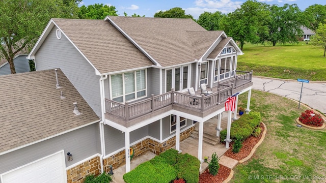 rear view of house featuring roof with shingles, a lawn, a balcony, and stone siding