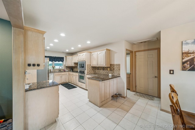 kitchen featuring decorative backsplash, light brown cabinetry, a sink, dark stone countertops, and appliances with stainless steel finishes