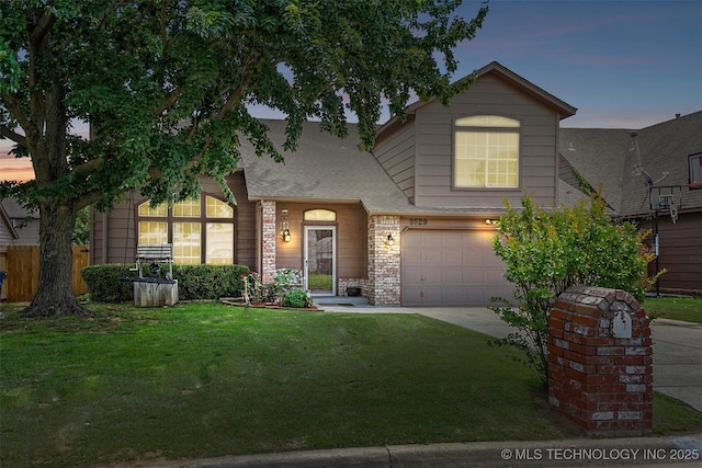 traditional-style house featuring a lawn, an attached garage, driveway, and roof with shingles