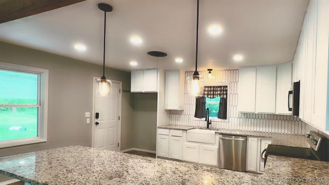 kitchen featuring a peninsula, white cabinetry, light stone counters, a sink, and appliances with stainless steel finishes