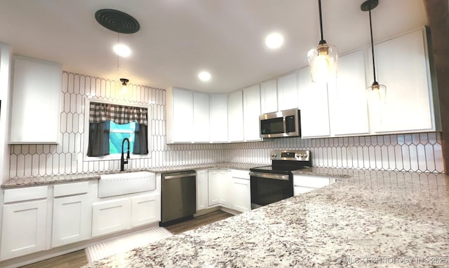 kitchen featuring light stone countertops, white cabinetry, a sink, appliances with stainless steel finishes, and decorative light fixtures