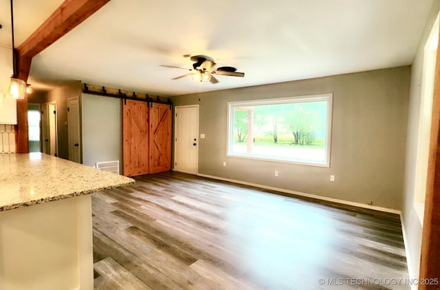 unfurnished living room featuring a barn door, baseboards, a ceiling fan, and wood finished floors