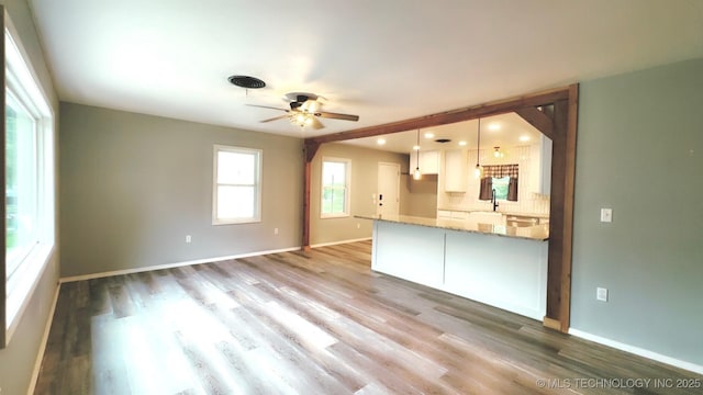 unfurnished living room with baseboards, a sink, ceiling fan, and wood finished floors
