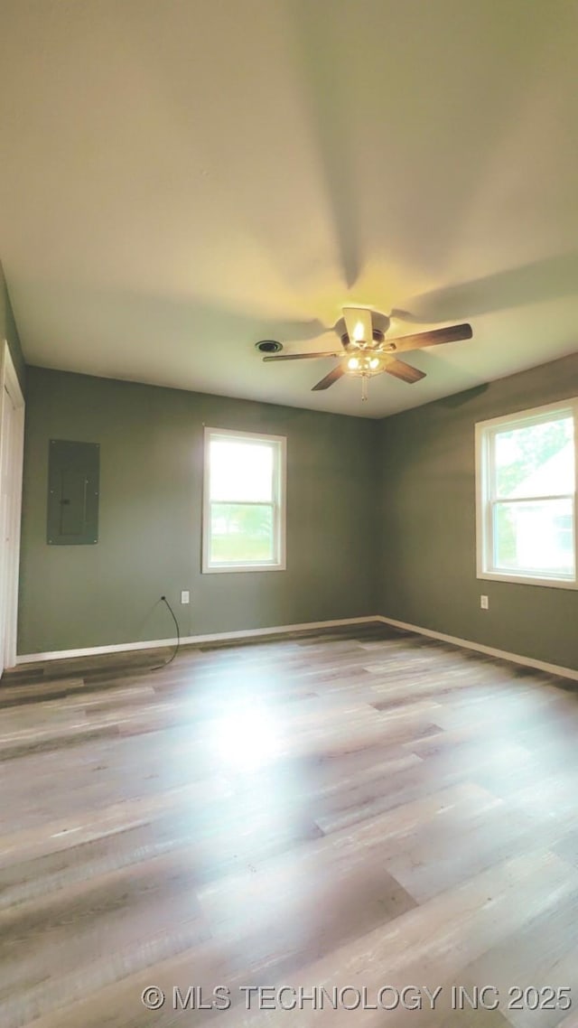 empty room with a ceiling fan, baseboards, a healthy amount of sunlight, and electric panel
