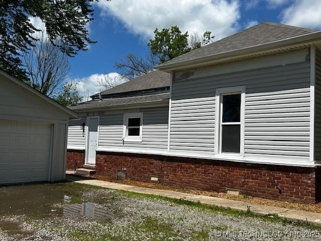 view of property exterior with a garage, entry steps, roof with shingles, and brick siding