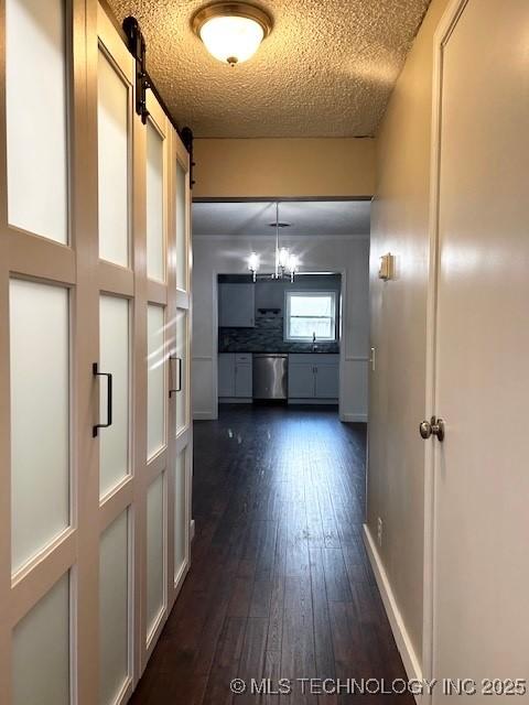 hall with baseboards, dark wood-style floors, a barn door, a textured ceiling, and a sink