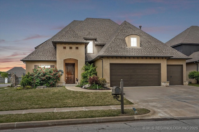 french country home with a lawn, stucco siding, a shingled roof, concrete driveway, and an attached garage