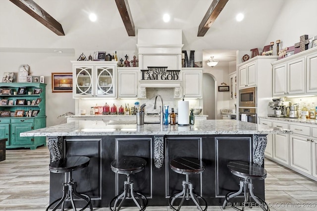 kitchen with decorative backsplash, a kitchen bar, appliances with stainless steel finishes, light stone countertops, and a center island with sink