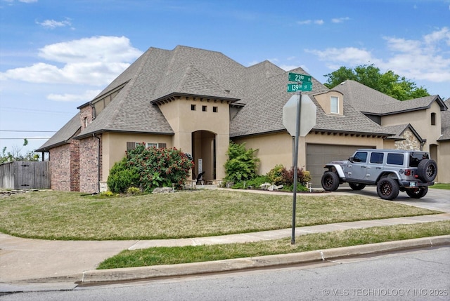 french country home featuring a garage, a front lawn, stucco siding, a shingled roof, and concrete driveway