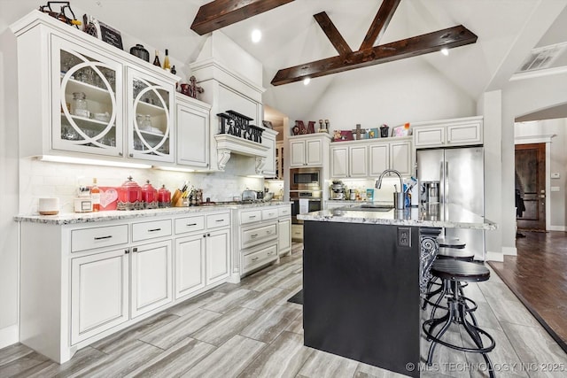 kitchen with stainless steel appliances, beam ceiling, light stone countertops, and a sink