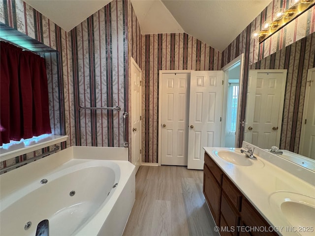full bathroom featuring a sink, wallpapered walls, a tub with jets, wood finished floors, and vaulted ceiling