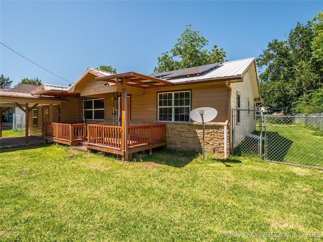 back of house with fence, a deck, stone siding, a lawn, and solar panels