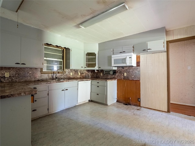 kitchen with dark countertops, tasteful backsplash, a sink, white appliances, and light floors