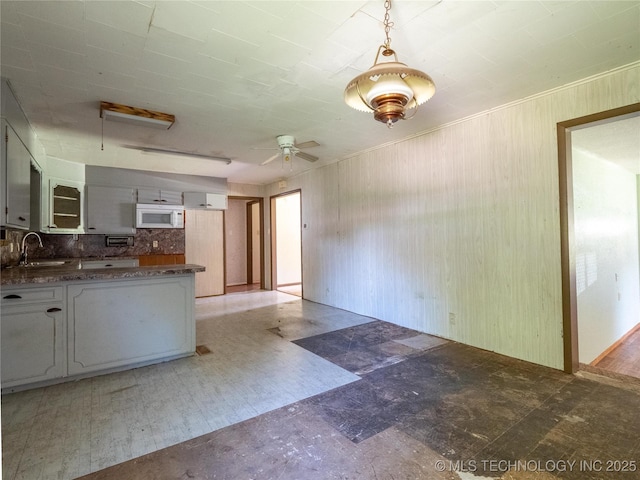 kitchen featuring a ceiling fan, tasteful backsplash, a sink, white microwave, and light floors