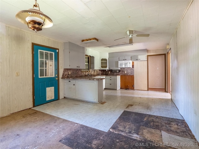 kitchen with dark countertops, white microwave, a peninsula, a ceiling fan, and light floors
