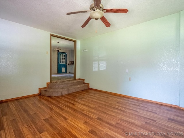 unfurnished room with light wood-style floors, baseboards, ceiling fan, and stairway