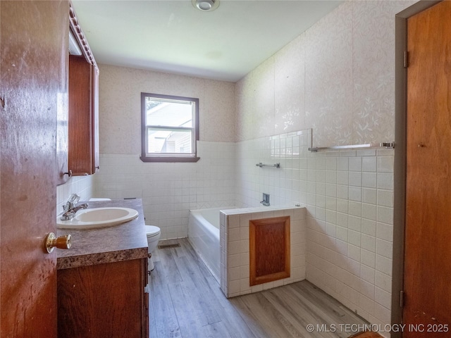 full bath with vanity, toilet, tile walls, wood finished floors, and a garden tub