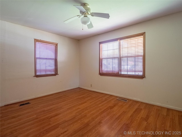 spare room with baseboards, a ceiling fan, light wood-type flooring, and visible vents