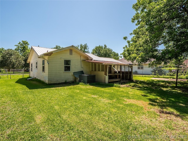 rear view of house with central AC unit, fence, a yard, and metal roof