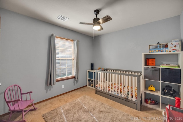 carpeted bedroom with a crib, baseboards, ceiling fan, and visible vents