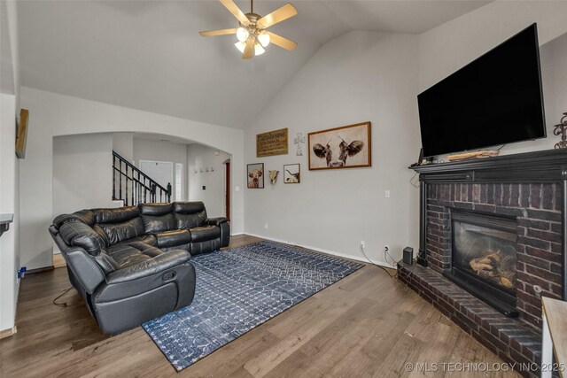 living area with ceiling fan, a brick fireplace, arched walkways, wood finished floors, and vaulted ceiling