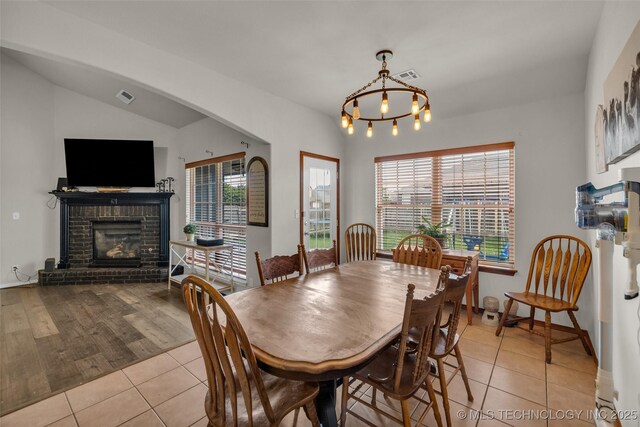 dining area with a brick fireplace, a notable chandelier, light tile patterned flooring, and visible vents
