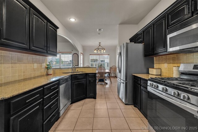 kitchen featuring tasteful backsplash, a sink, a notable chandelier, dark cabinets, and stainless steel appliances