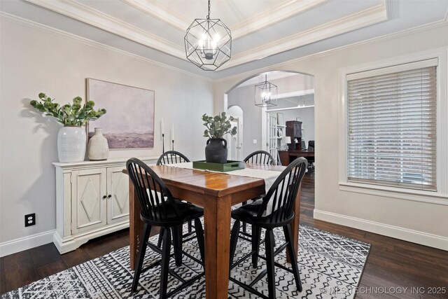 dining area featuring crown molding, baseboards, dark wood-type flooring, a raised ceiling, and arched walkways