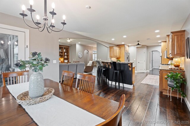dining space with dark wood-style flooring, arched walkways, a chandelier, and recessed lighting