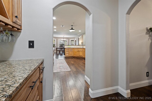 hall featuring dark wood-style flooring, arched walkways, and baseboards