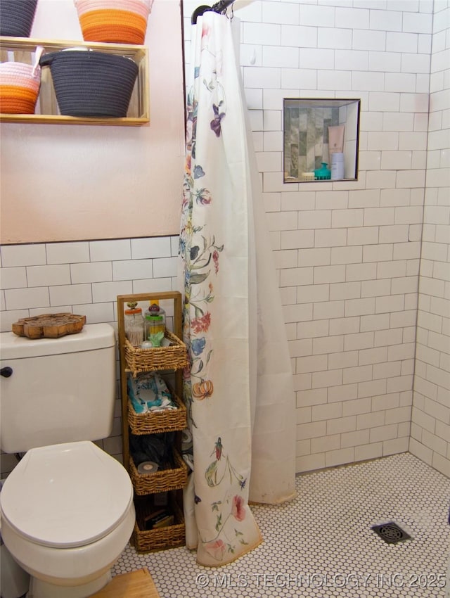 full bathroom with tile patterned flooring, wainscoting, toilet, tile walls, and a stall shower